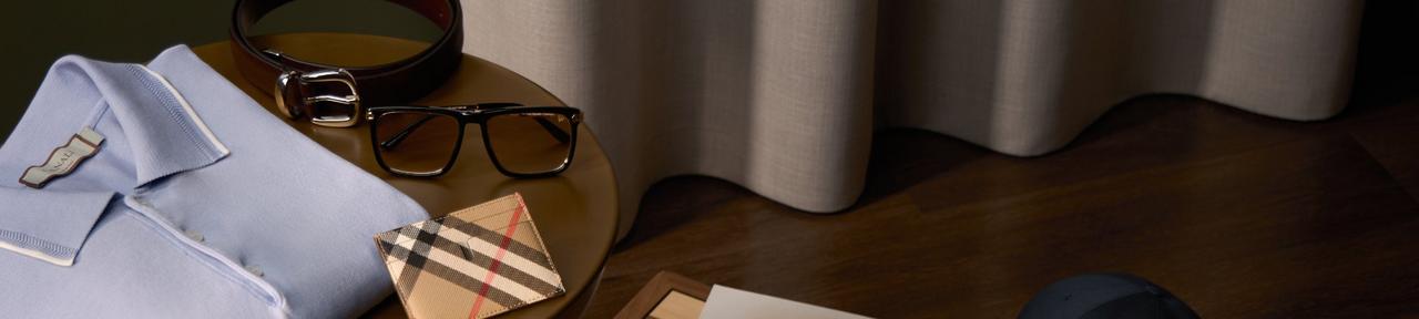 men's accessories, including a light blue collared shirt, a leather belt, eyeglasses, a patterned wallet, and a pair of shoes