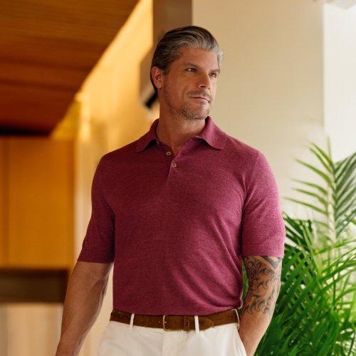 Un homme portant un polo rouge bordeaux, un pantalon blanc cassé et une ceinture brune