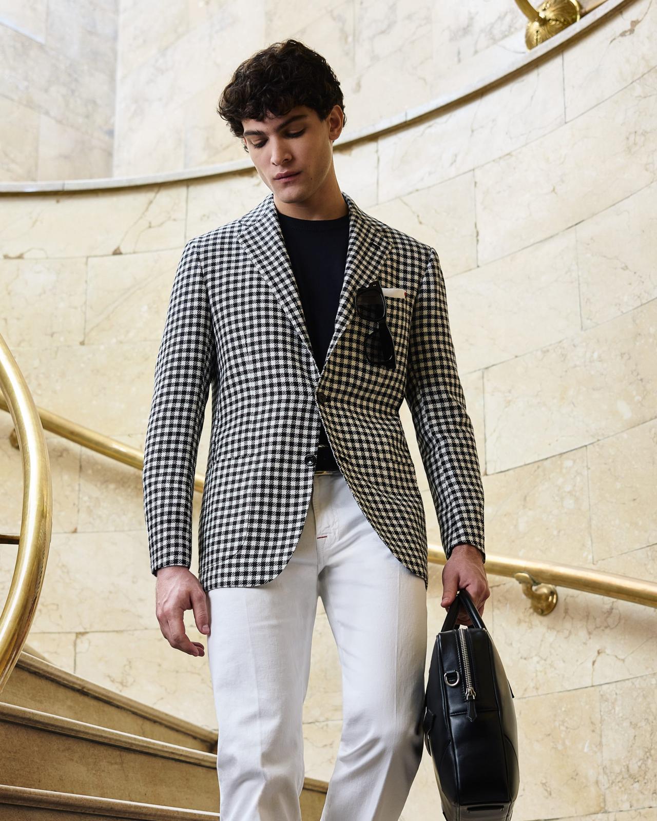 Male model wearing a black and white patterned Kiton jacket styled with white pants and leather derbies