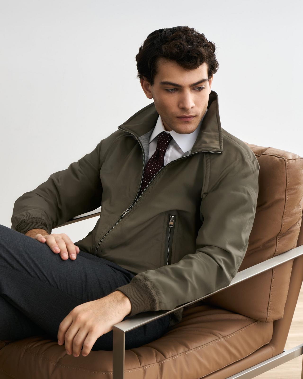 Un mannequin masculin se détend en portant une veste Tom Ford vert forêt, agencée à une chemise habillée blanche et une cravate à motifs