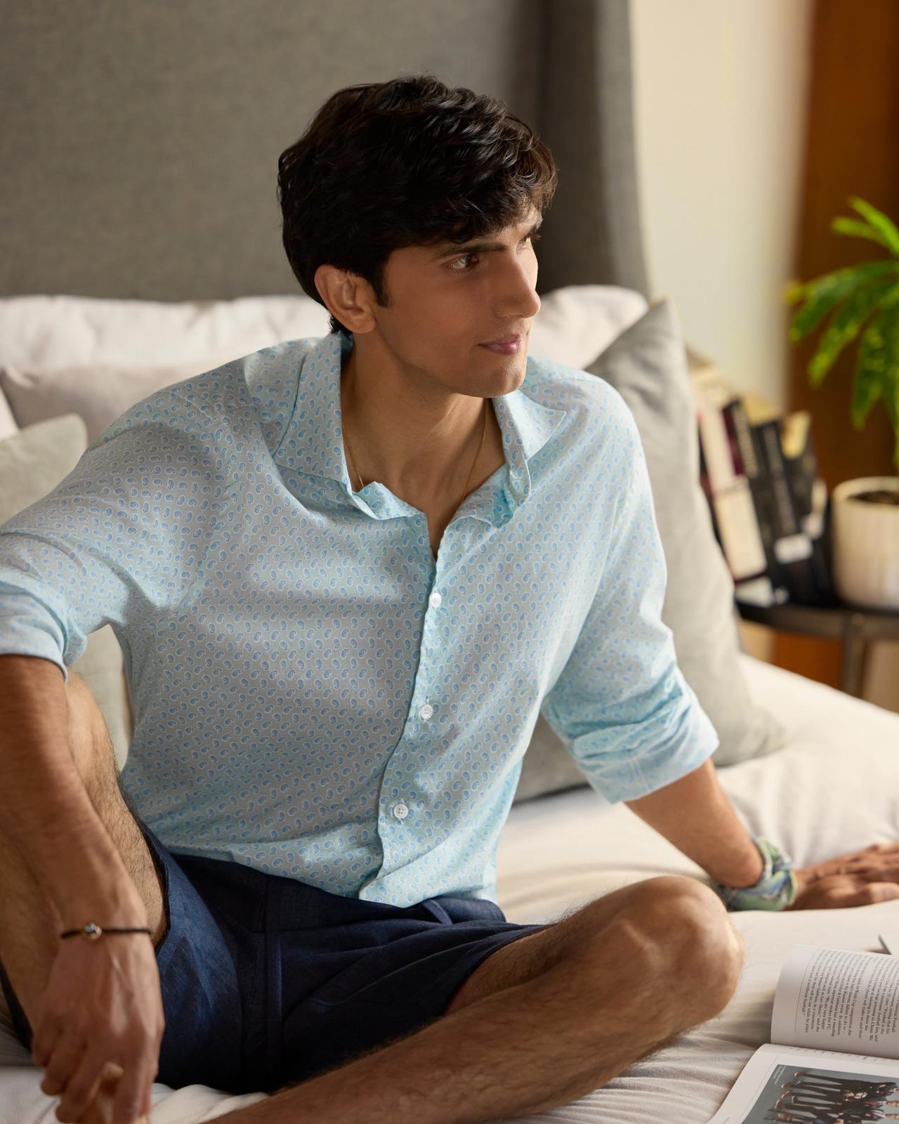 A man wearing a light blue casual shirt with navy blue shorts