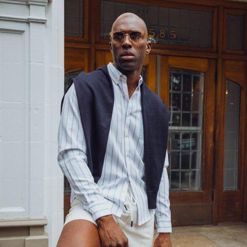 Male fashion model wearing a light blue and white striped button-up shirt, paired with a navy blue vest and white shorts