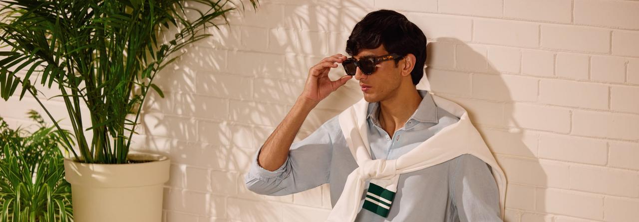 Un homme portant une chemise gris pâle avec un chandail léger blanc cassé sur les épaules