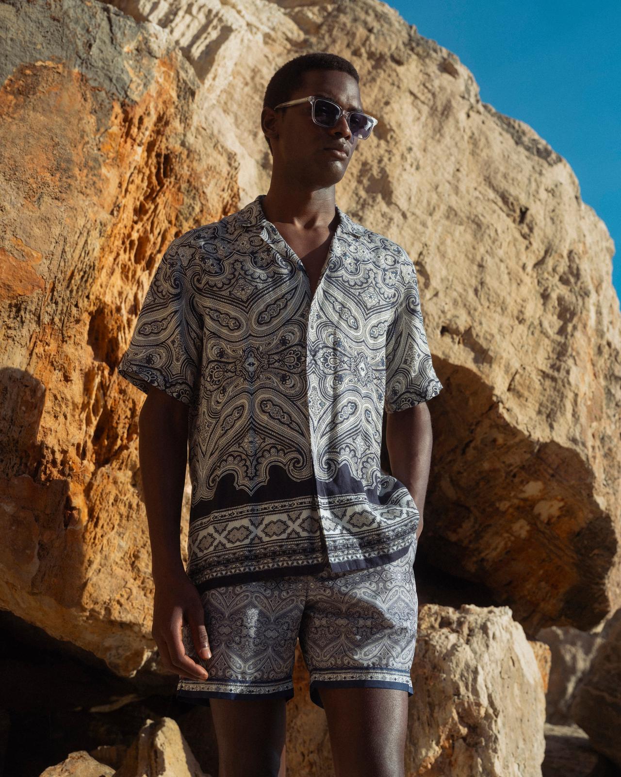 A man wearing a dark blue and white printed linen shirt and shorts