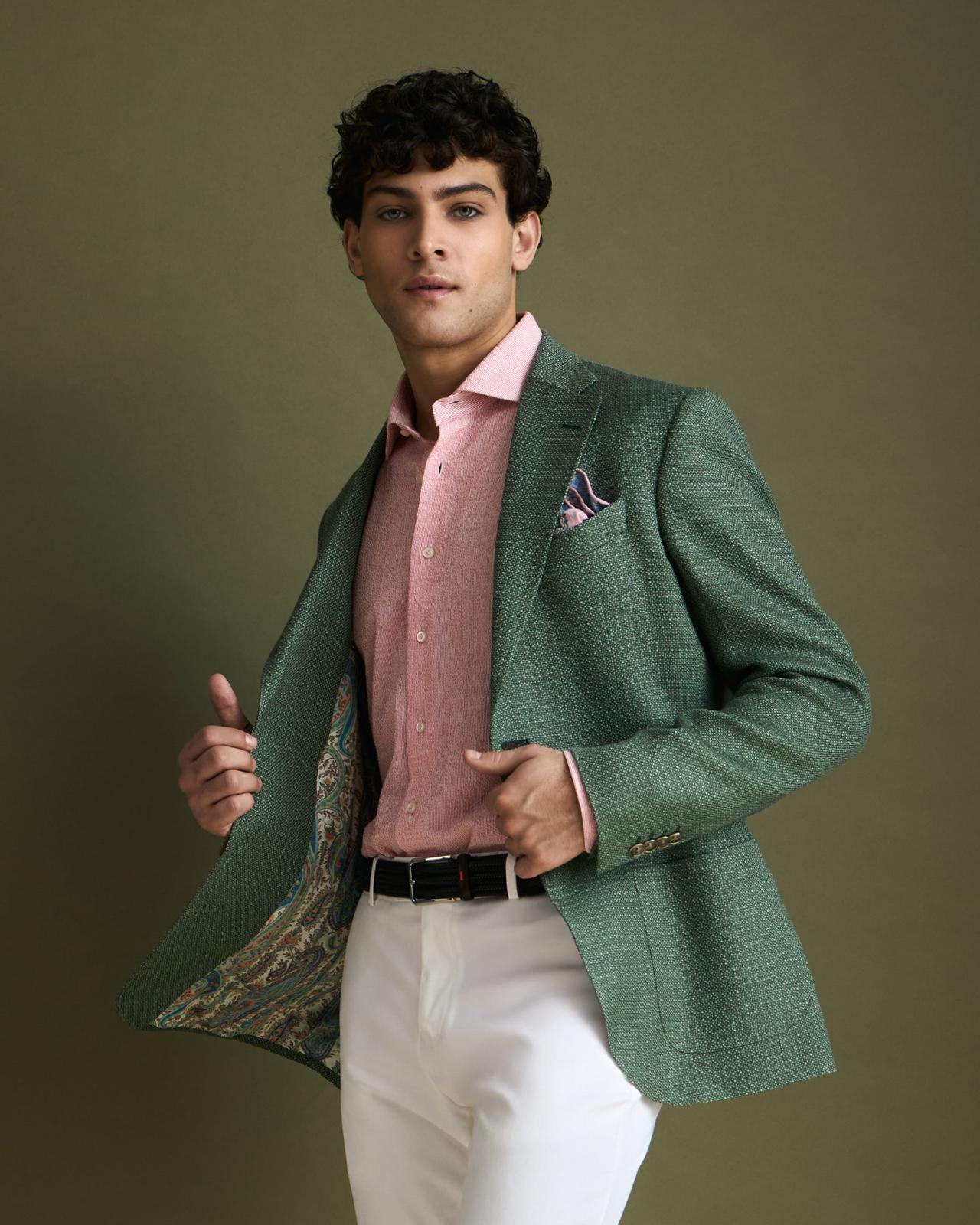 A man wearing a dark green sport jacket with pink dress shirt and an Off-white pant