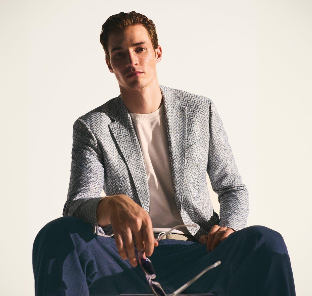 Un homme portant une veste sport à motif rayé gris et noir avec un pantalon bleu marine