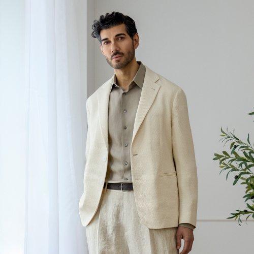 A man wearing an off-white suit with light olive shirt and dark brown belt