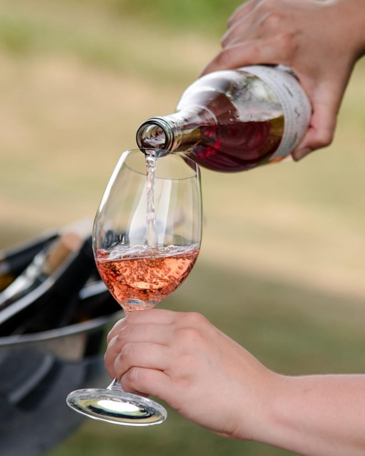 a person pouring a glass of rosé wine from a bottle