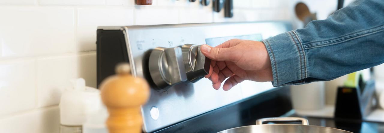A person adjusting the temperature control knob on a stainless steel electric stove in a modern kitchen