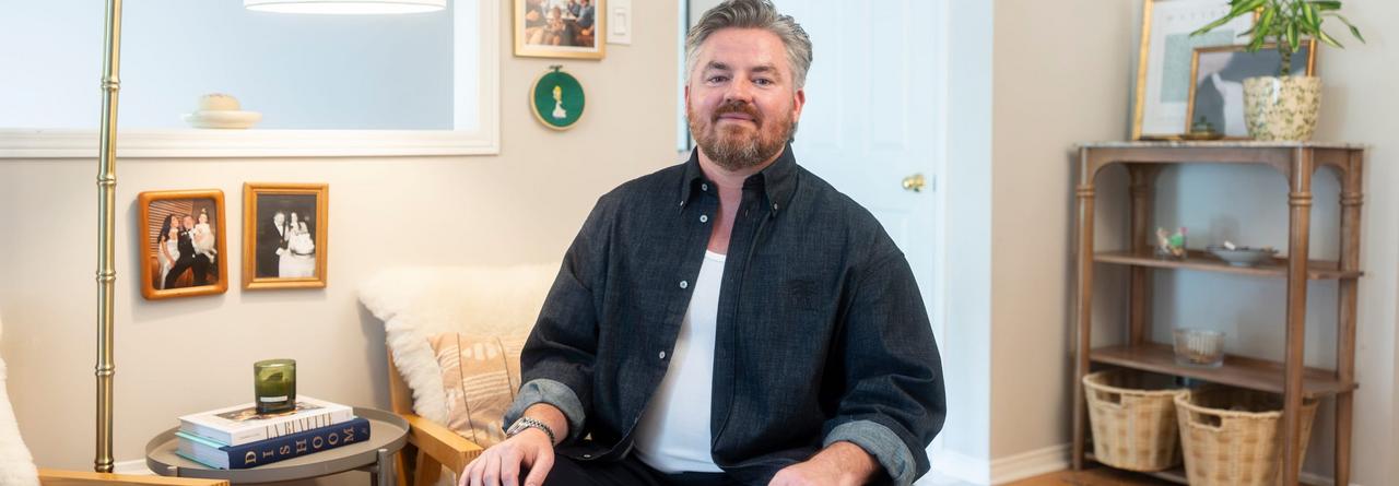 A person seated in a cozy, modern living room with neutral tones, framed family photos