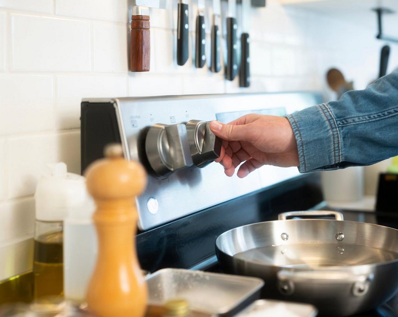 A person adjusting the temperature control knob on a stainless steel electric stove in a modern kitchen