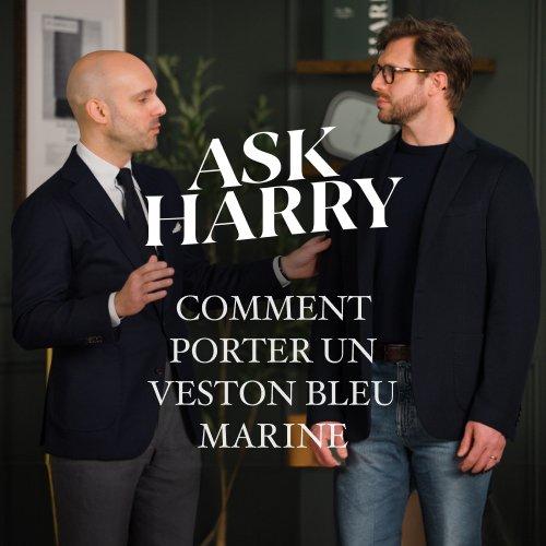 Un homme portant un complet gris foncé avec un t-shirt à col rond blanc cassé.