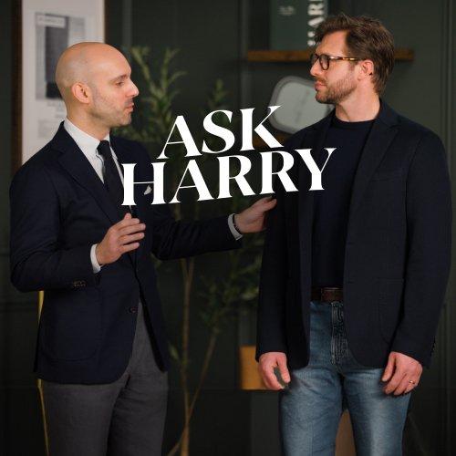 Un homme portant un complet gris foncé avec un t-shirt à col rond blanc cassé.