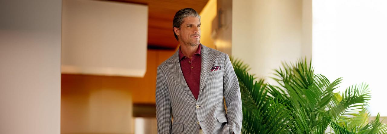 A man wearing a light grey and black blazer with red polo and silk red and white pocket square
