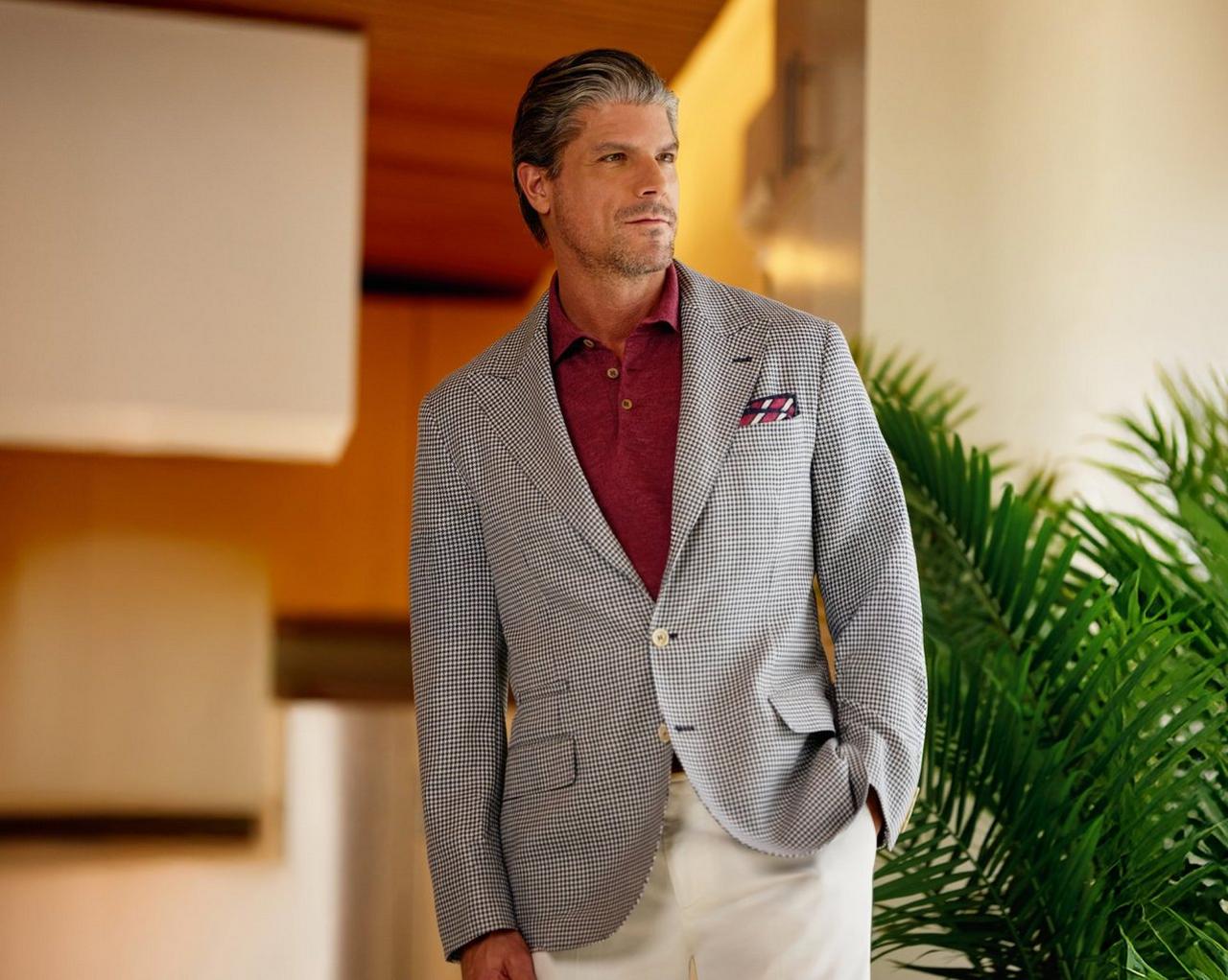 Un homme portant un veston gris clair et noir avec un polo rouge et une pochette en soie rouge et blanche