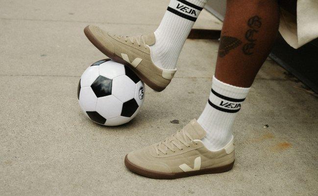 Model in beige VEJA Volley suede sneakers with white logo socks, standing beside a classic black-and-white soccer ball