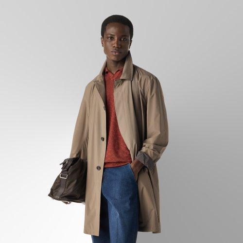 Un homme portant un manteau beige avec un t-shirt à col rond couleur rouille et un pantalon bleu foncé