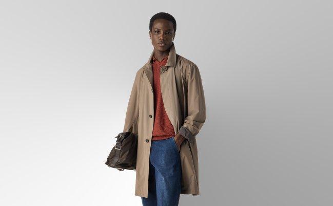 A man wearing a beige coat with rust c-neck t-shirt and dark blue pant