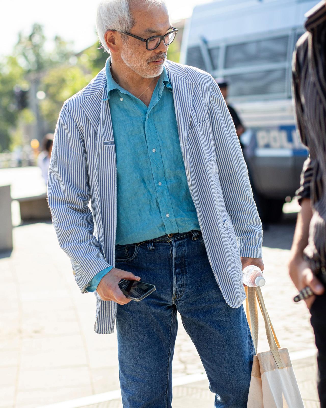 A man featuring a blue button-up shirt, striped blazer, and dark jeans