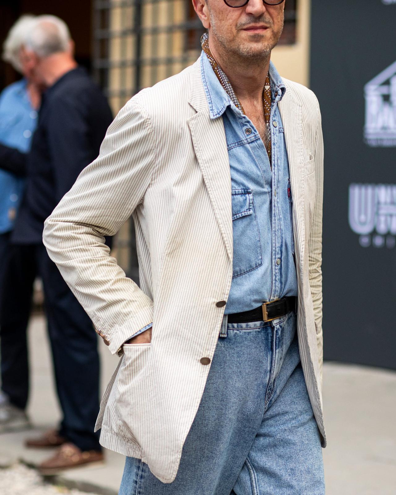 Un homme portant un veston en velours côtelé beige pâle par-dessus une chemise en denim bleue, agencé à un jean taille haute et une ceinture noire