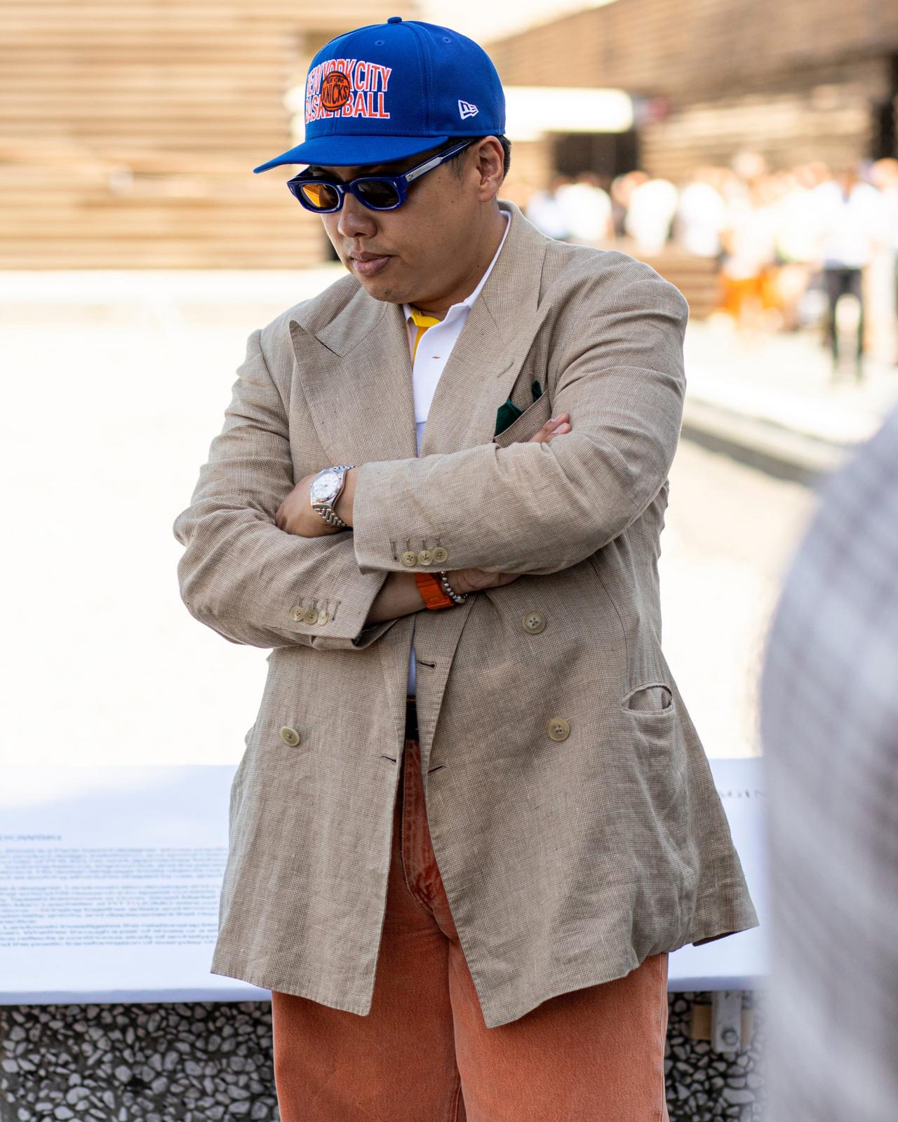 A man wearing a beige double-breasted blazer over a white shirt, paired with rust-colored trousers 