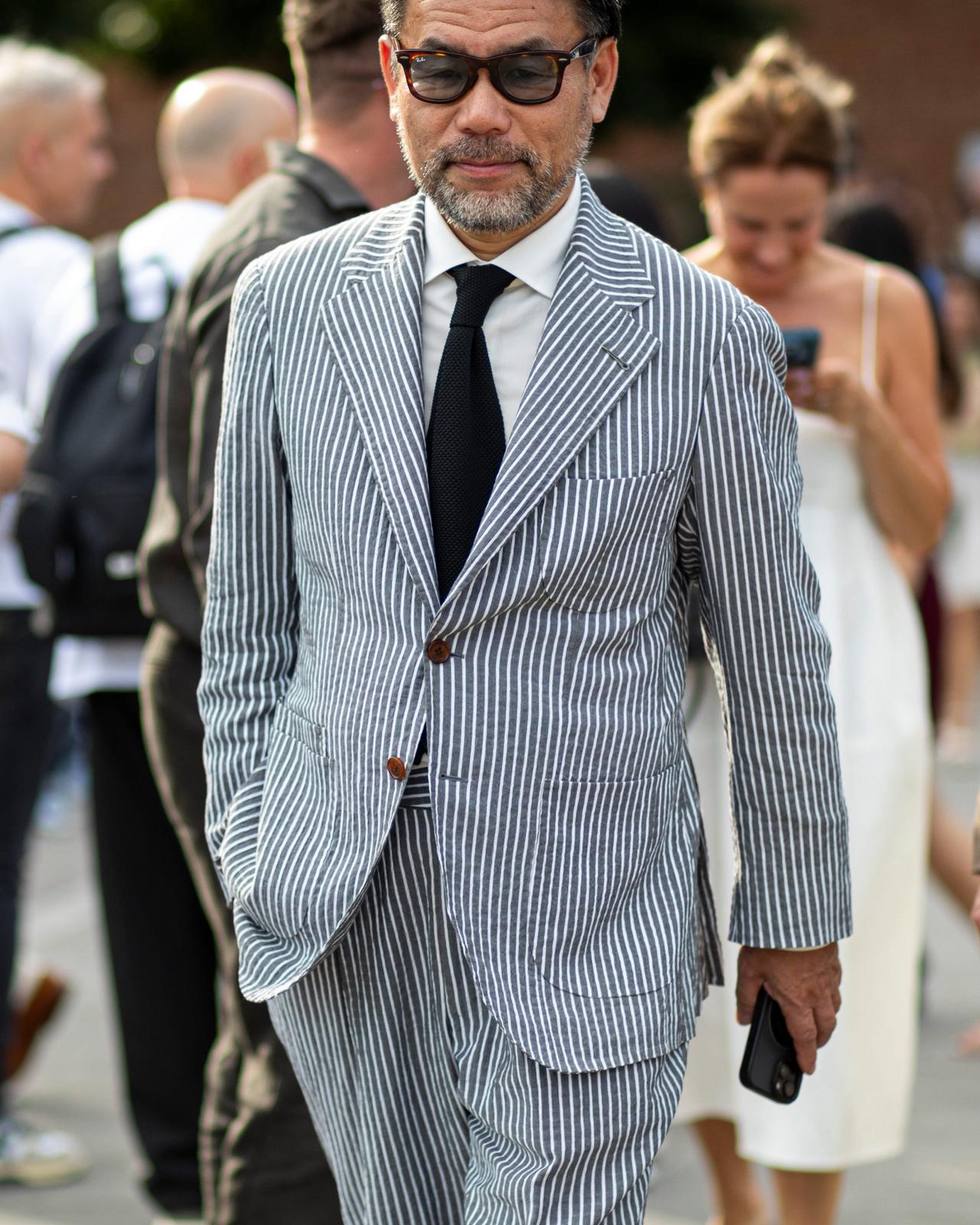 A man wearing a light gray pinstripe suit paired with a white dress shirt and a black tie 