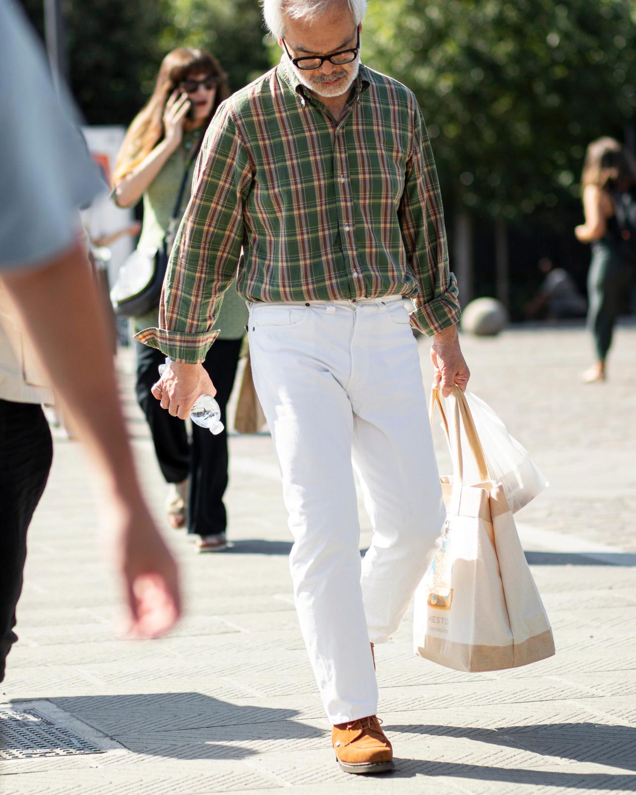 A man wearing a green plaid shirt, white trousers, and brown leather shoes