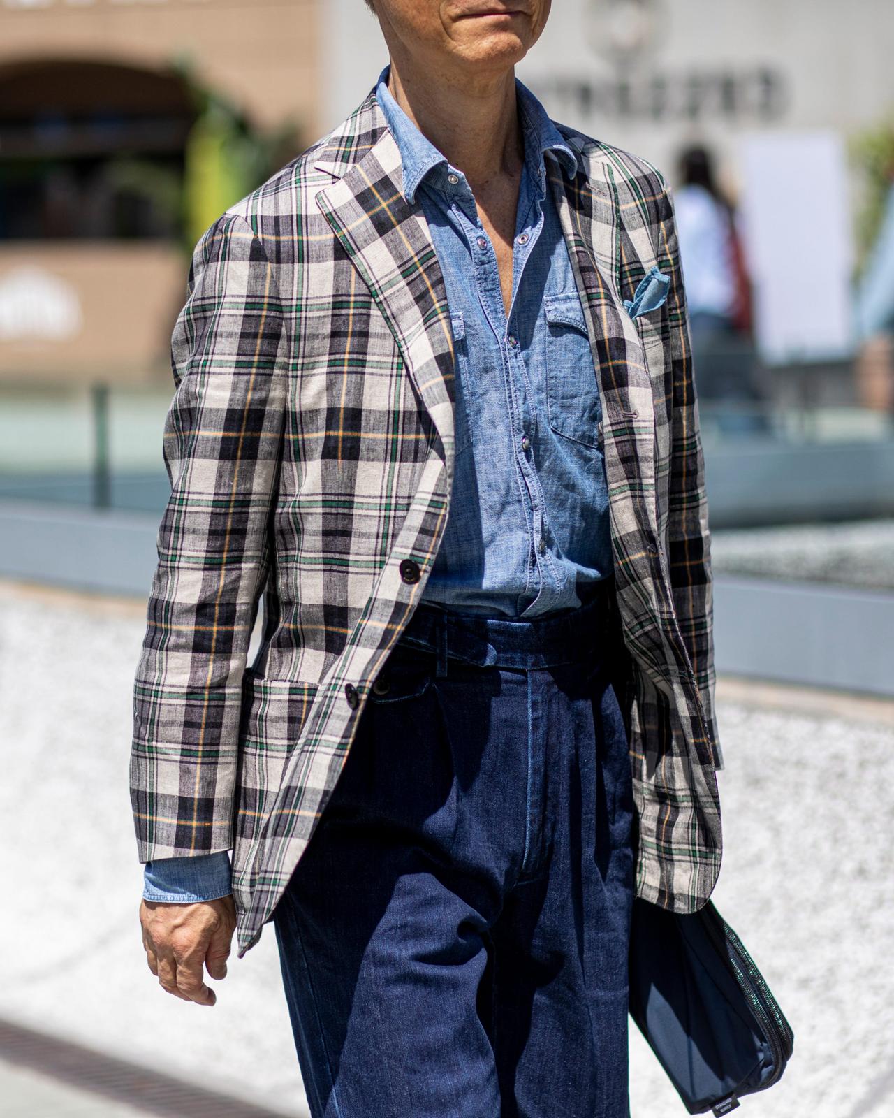 Un homme portant un veston à carreaux pâles par-dessus une chemise bleue à boutons, agencé à un pantalon bleu marine foncé à taille haute