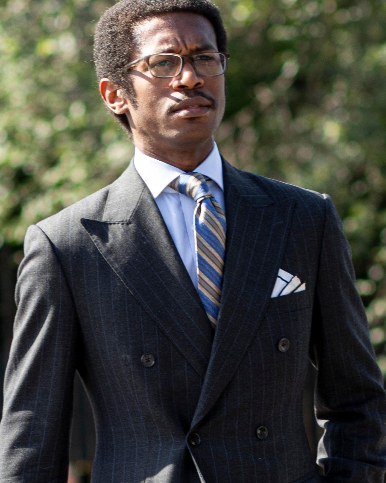 A man wearing a charcoal grey double-breasted suit paired with a light blue dress shirt and a striped tie
