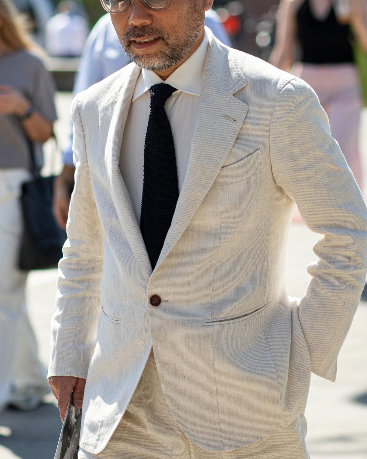 A man wearing a light beige linen suit paired with a white dress shirt and a dark textured tie