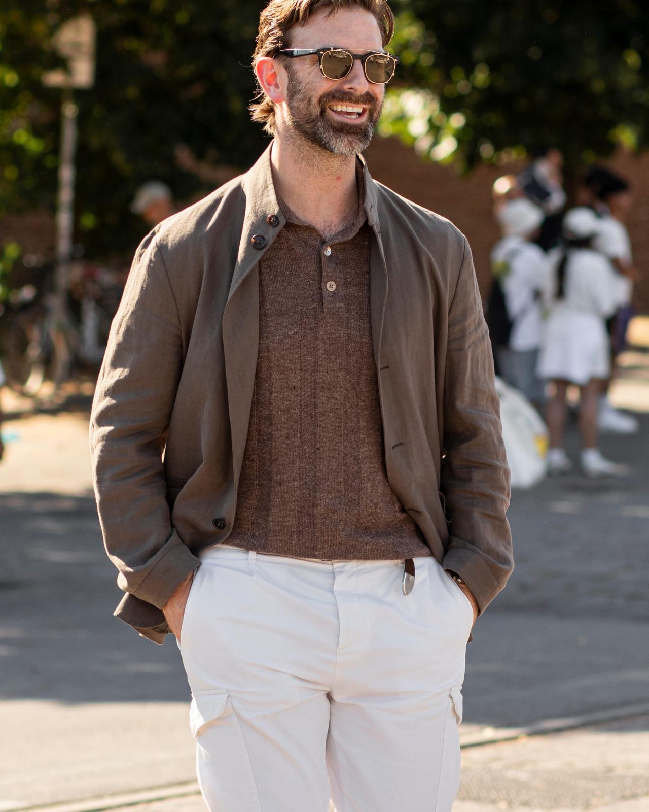 A man in a brown buttoned shirt layered under a taupe blazer, paired with white trousers