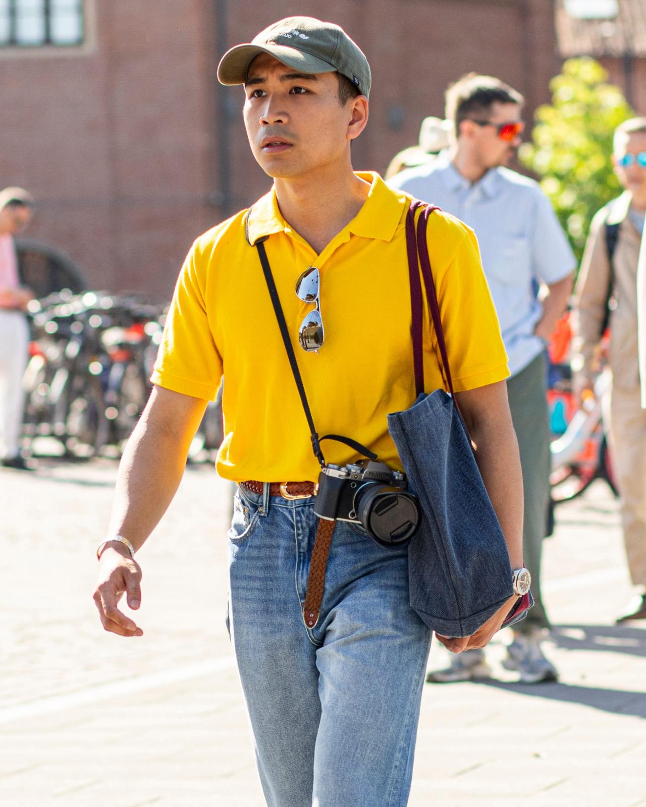 A man featuring a bright yellow polo shirt, blue jeans, and a camera slung over his shoulder