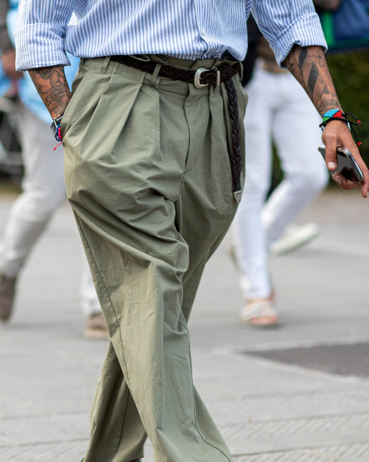 A man wearing olive green pleated trousers paired with a blue and white striped shirt