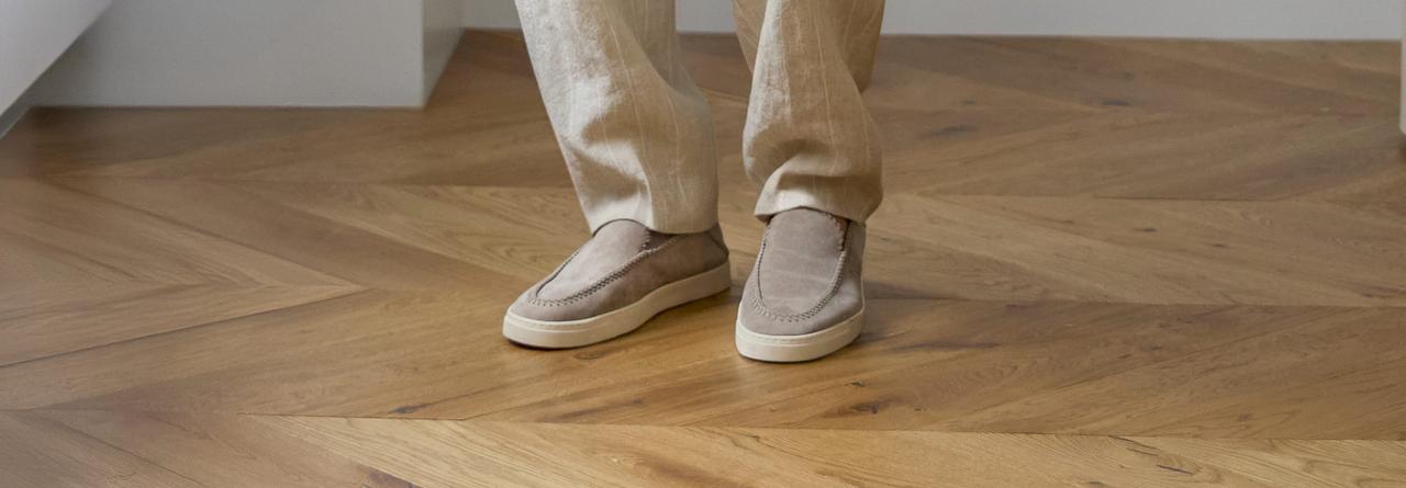 A man wearing beige suede slip-on sneakers paired with light-colored linen trousers