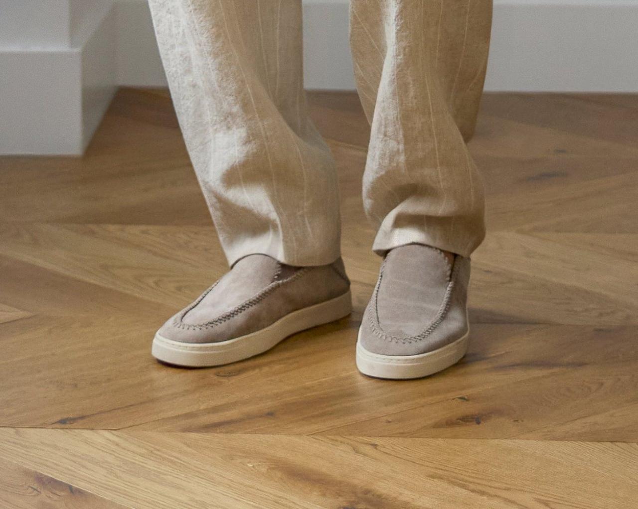 A man wearing beige suede slip-on sneakers paired with light-colored linen trousers