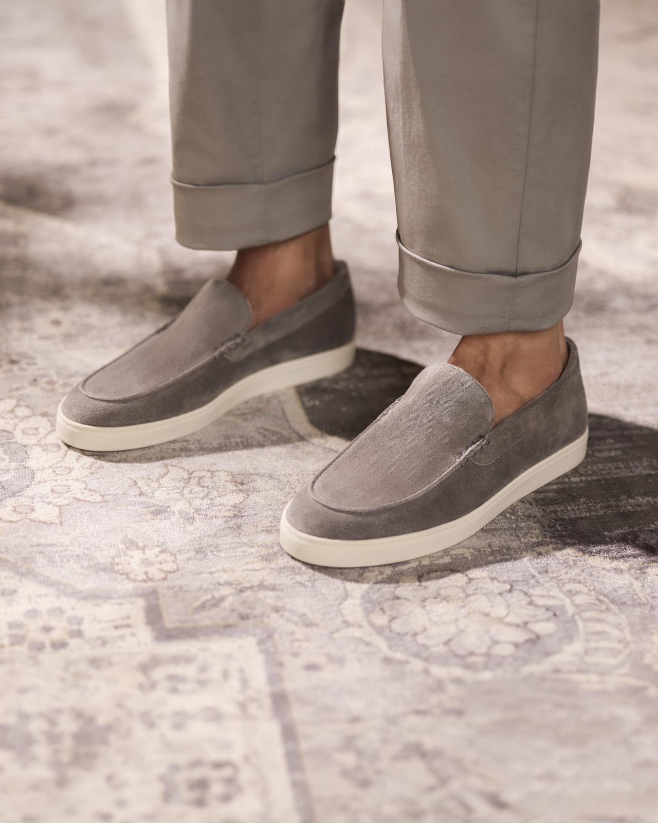 Un homme portant des mocassins en suède gris pâle, assortis à un pantalon à revers