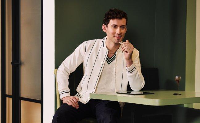 A man wearing an off-white sweater with black pants 