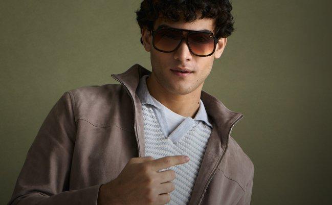 Un homme portant une surchemise brun-gris, un t-shirt en maille et un pantalon gris foncé