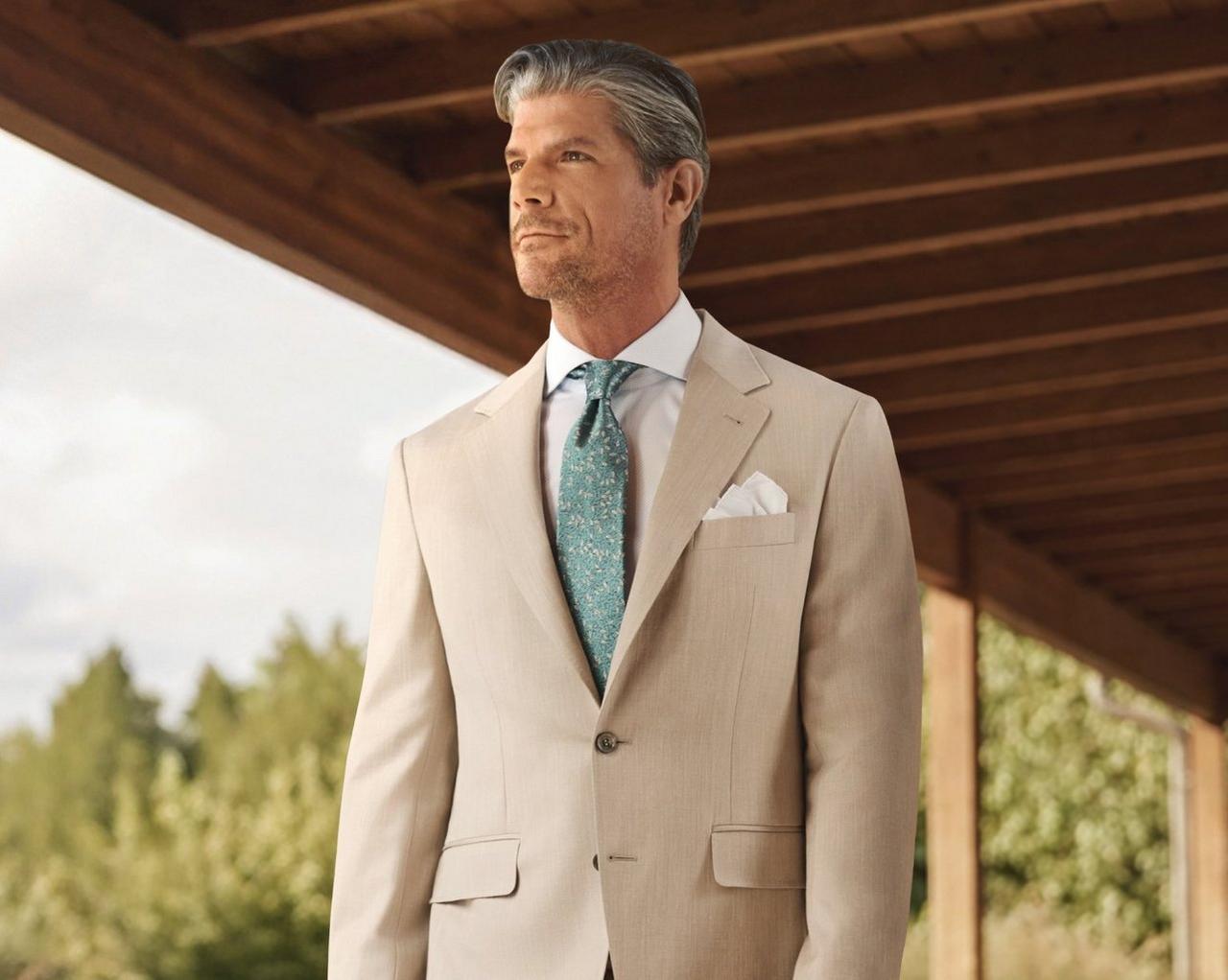 A man wearing a cream suit with white shirt, pocket square and sea green tie