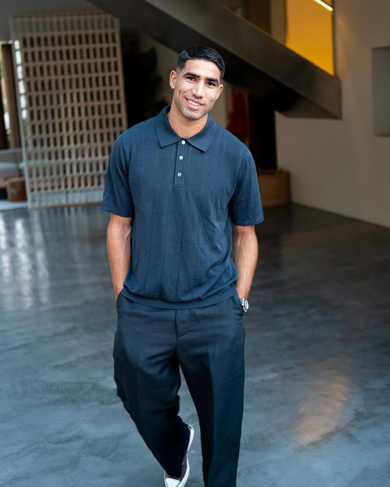 Achraf portant un polo en tricot bleu foncé avec un pantalon en lin