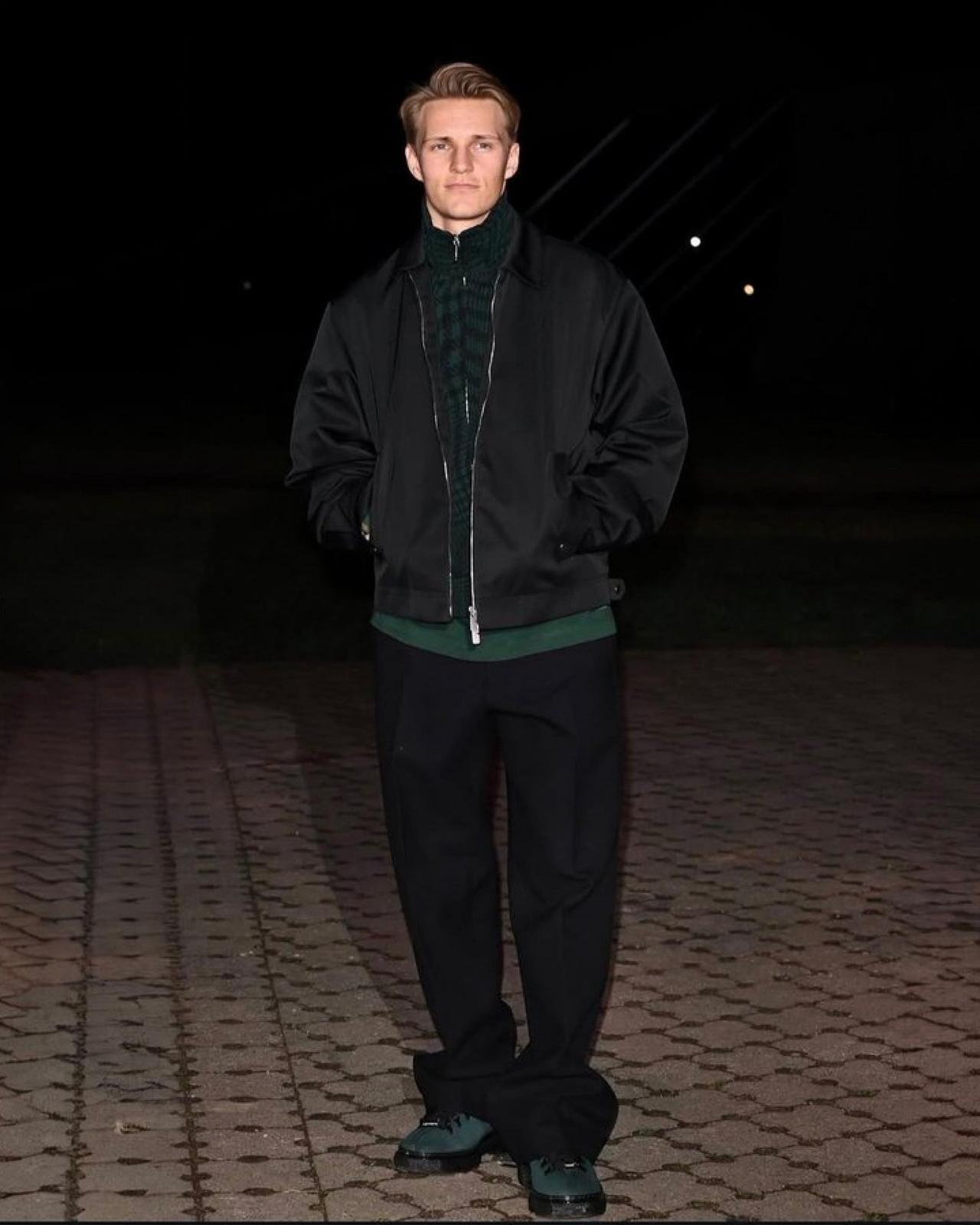 Martin wearing a black bomber jacket, green t-shirt with baggy trousers and lace-up sneakers