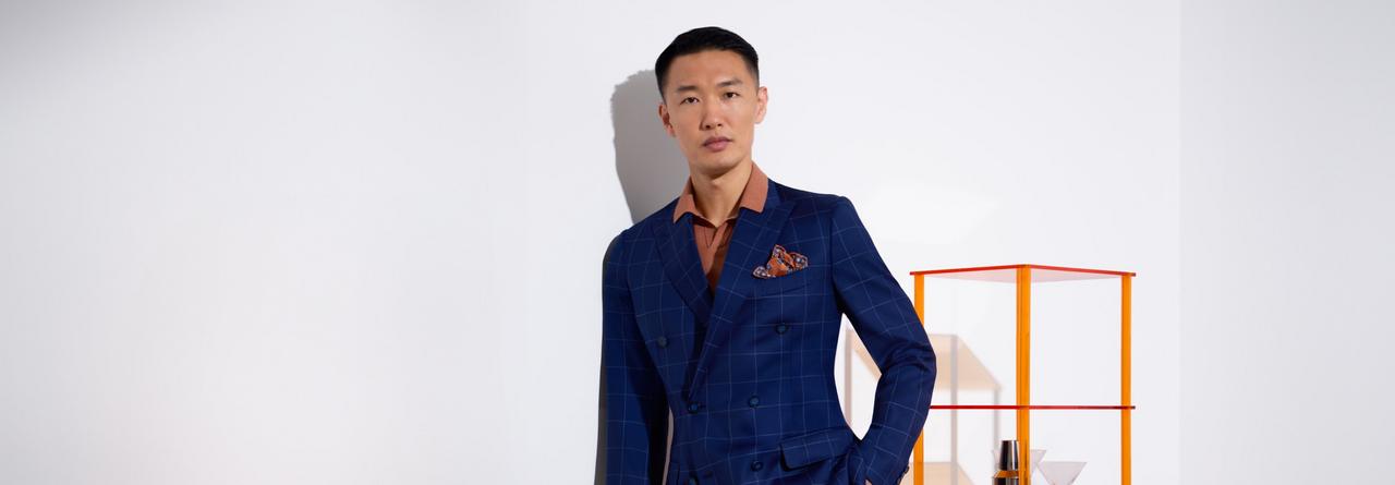 A man wearing a very dark blue suit with rust colored shirt and rust printed pocket square