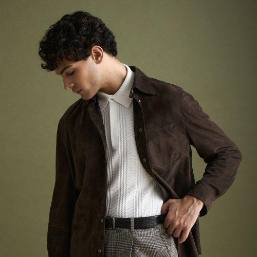 Un homme portant une surchemise brun chocolat foncé, un polo et un pantalon gris à carreaux