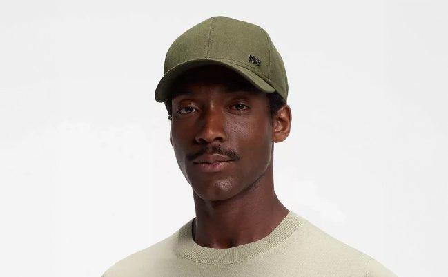 A man wearing tan logo cap paired with a light-colored crew-neck sweater