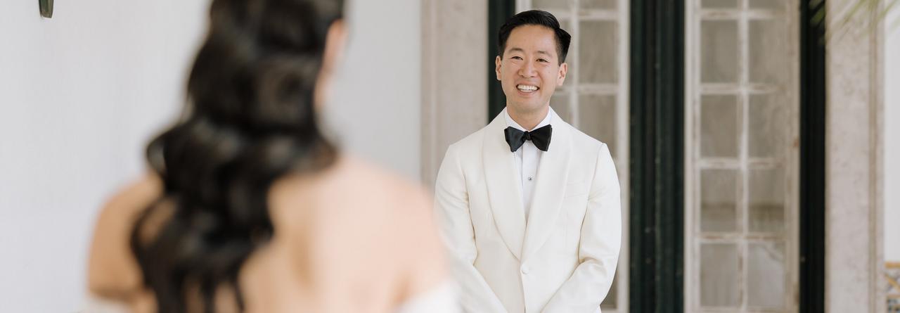 Un marié vêtu d’un smoking blanc avec un nœud papillon noir, se tenant devant une mariée