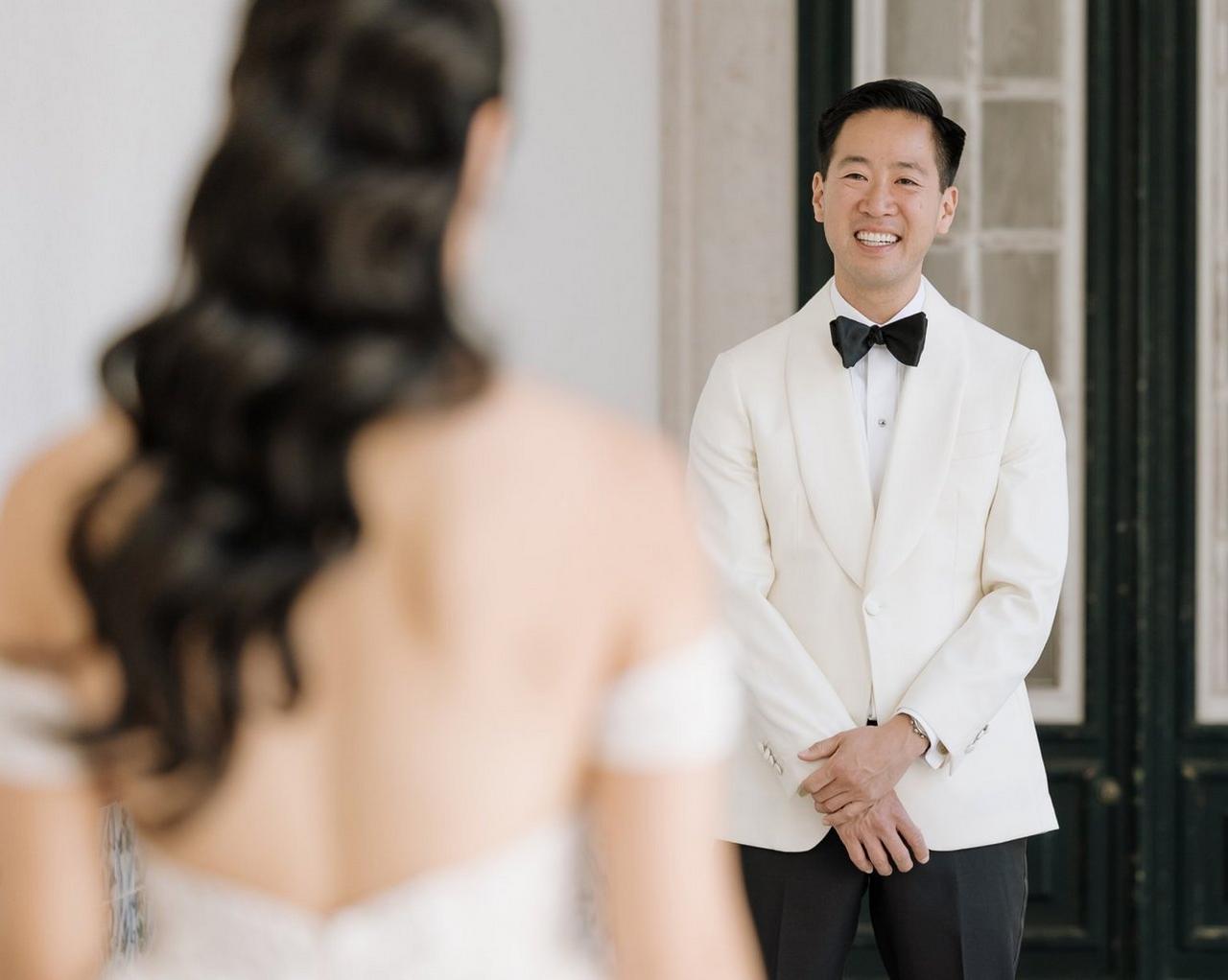 Un marié vêtu d’un smoking blanc avec un nœud papillon noir, se tenant devant une mariée