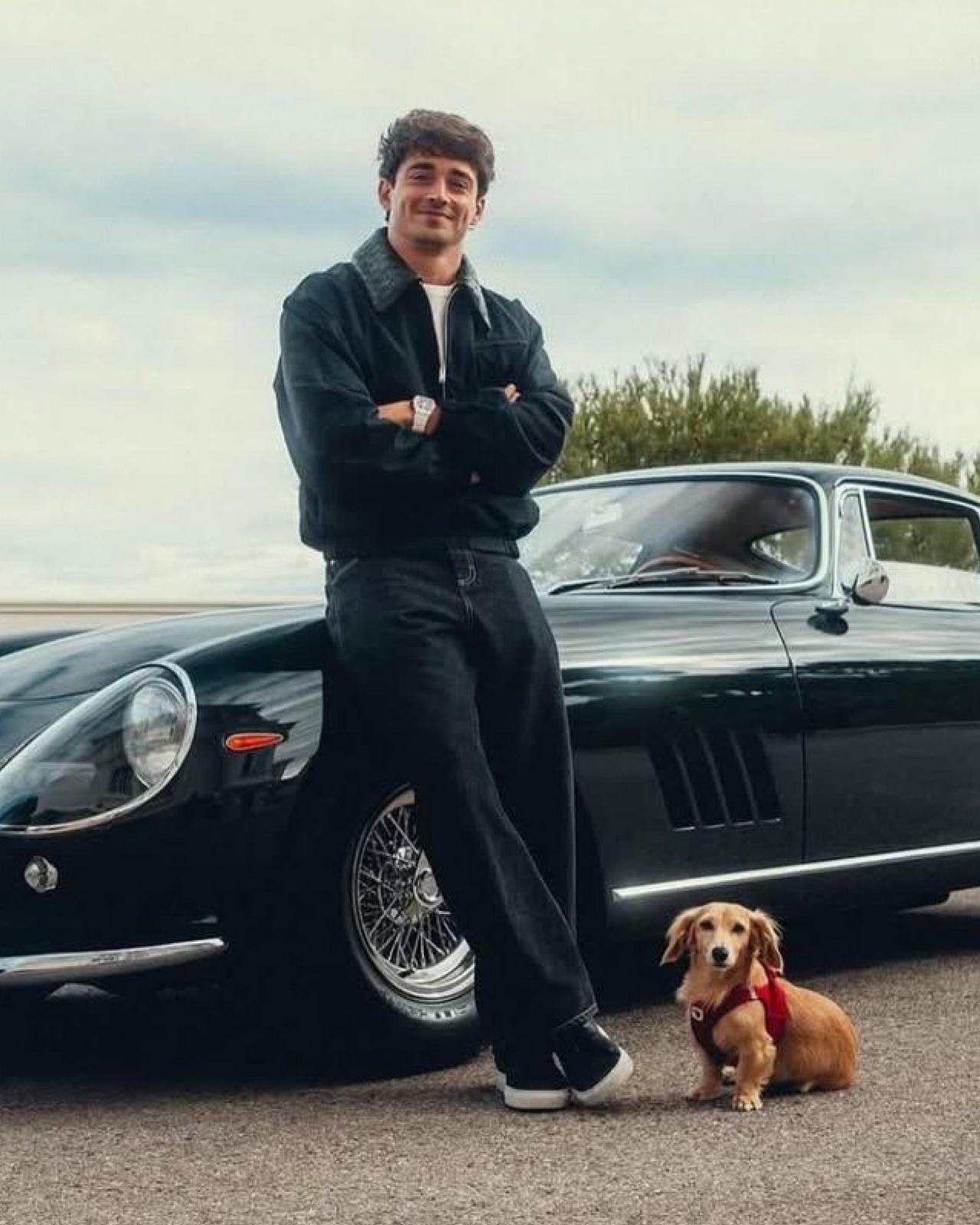 Charles Leclerc wearing a black jacket with white t-shirt and dark jeans standing with his dog