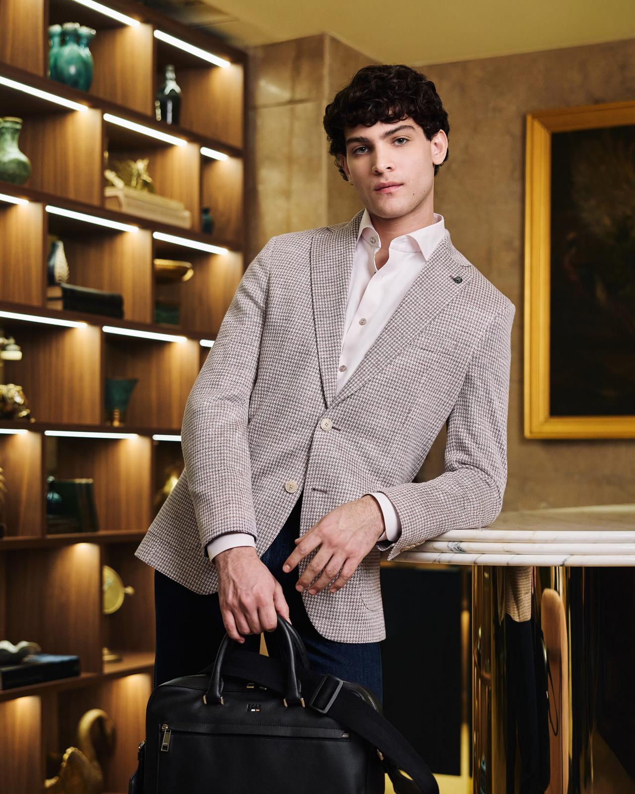 Mannequin homme portant un veston sport texturé avec une chemise habillée blanche, un pantalon marine et un sac de travail en cuir noir