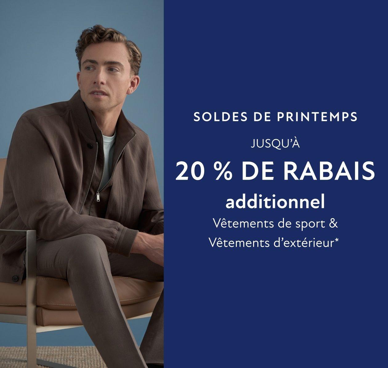 Un homme portant une veste brun foncé légère, un t-shirt bleu clair et un pantalon gris-brun