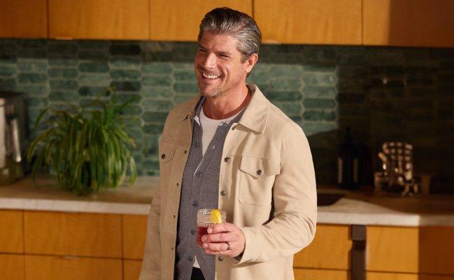 Un homme portant une veste crème pâle avec un chandail gris et un t-shirt blanc